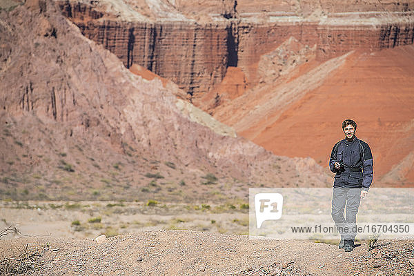 Man in motorcycle gear  standing in front of red sandstone formations