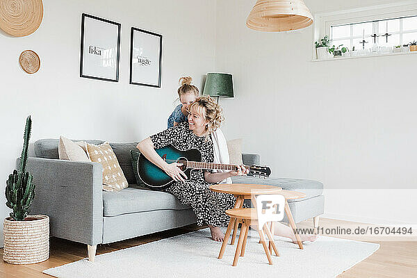 Tochter klettert auf Mutter  während sie zu Hause Gitarre spielt