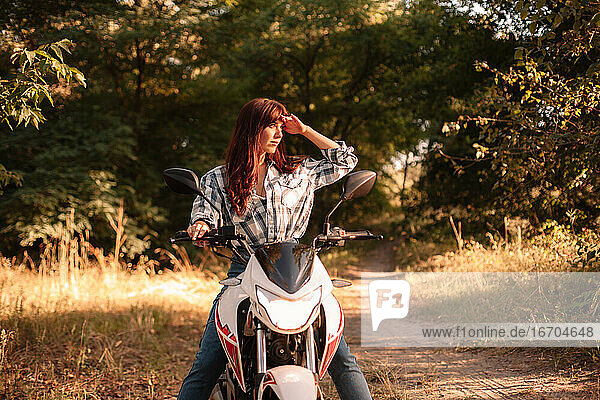 Junge Frau schützt ihre Augen beim Motorradfahren auf einem unbefestigten Weg
