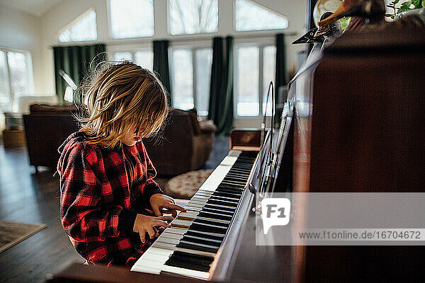 Kleiner Junge mit unordentlichem Haar spielt Klavier