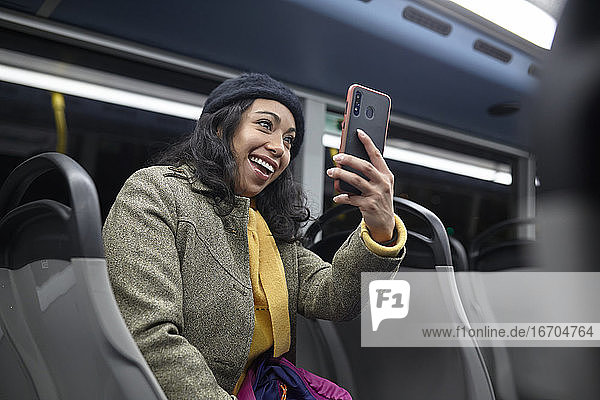 Lächelnde Frau  die nachts in einem öffentlichen Bus sitzt und ihr Handy benutzt