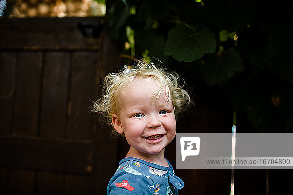Blonde zwei Jahre alten Jungen lächelnd für die Kamera stehend in Yard