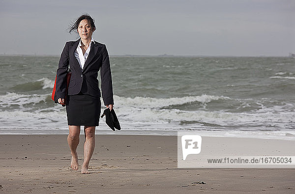 business woman walking on empty beach holding her shoes