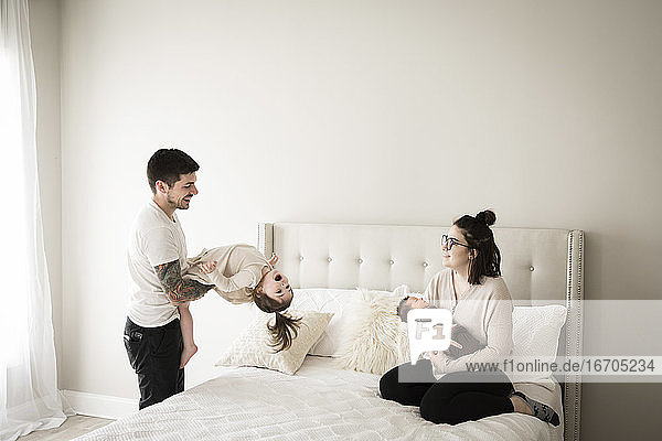 Happy Millennial Family Plays Together on White Bed at Home