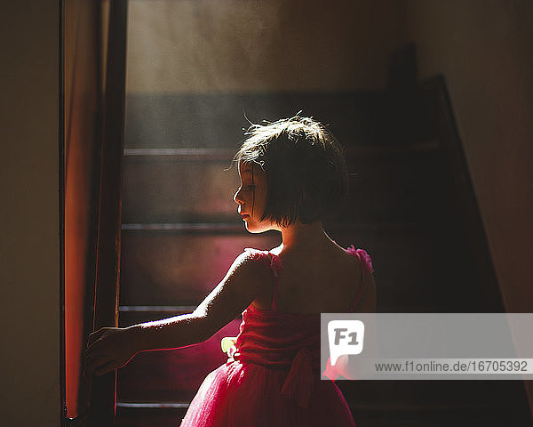 Ein anmutiges Kind steht in dunstigem Licht auf einer dunklen Treppe in einem ausgefallenen Kleid