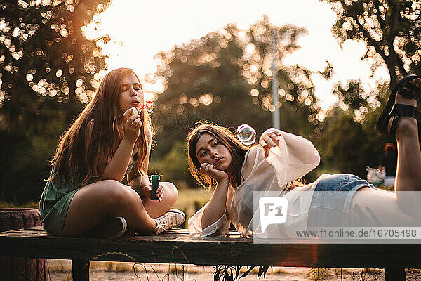Freundinnen spielen mit Blasen beim Entspannen im Park im Sommer