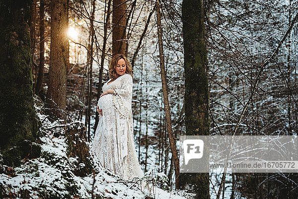 Vorderansicht einer schwangeren Frau im Wald mit der Sonne im Rücken