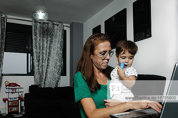 Woman with little kid on knees using laptop at home