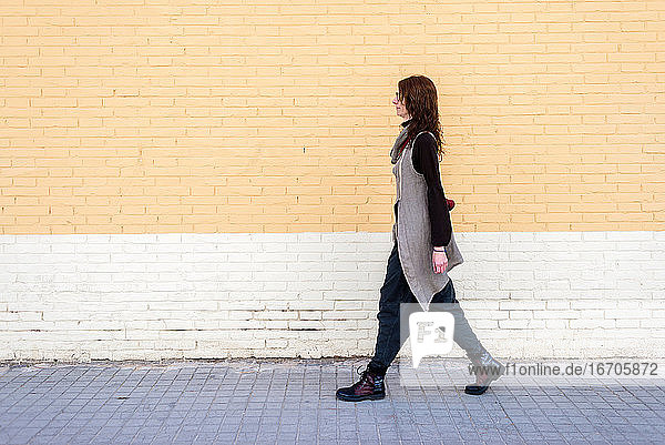 Young beautiful woman with eyeglasses walking against bricked wall .