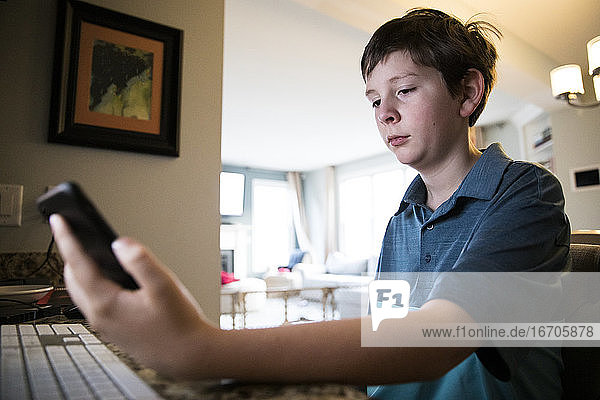 Low View of Tween Boy at Computer Desk Reading Texts on iPhone