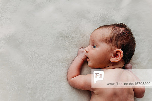 Newborn baby laying on a white blanket and looking to the side