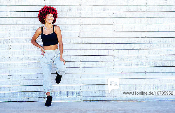 Woman with red afro hair standing on a white wall.