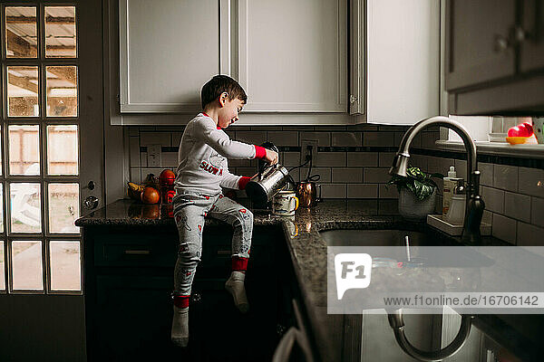 Kleiner Junge gießt Milch in eine Tasse Kaffee auf dem Küchentisch