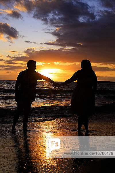 Ein junges Paar geht bei Sonnenuntergang am Strand spazieren