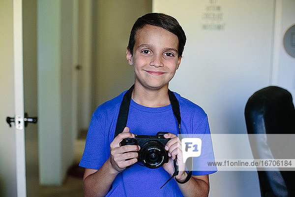 Portrait of a happy boy in a blue shirt holding a camera