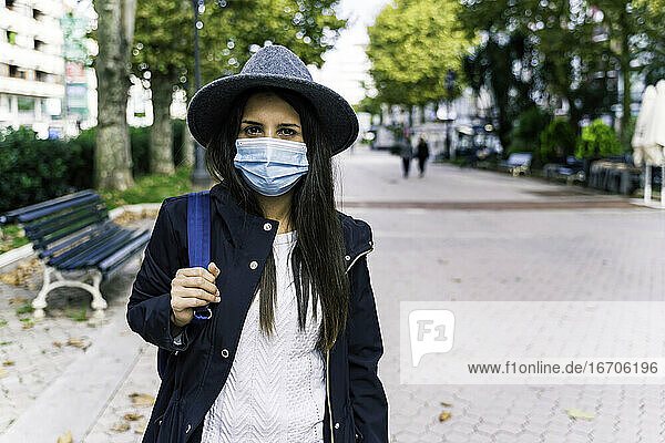 Schönes junges Mädchen mit Hut und Maske in der Stadt stehend