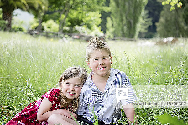 Junge und Mädchen sitzen im grünen Gras und schauen in die Kamera