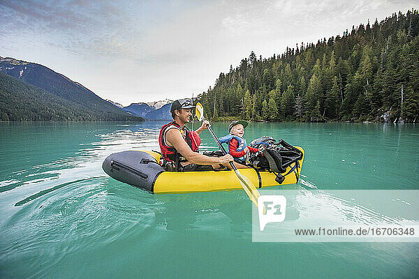 Vater und Sohn lachen  genießen eine Paddeltour auf einem türkisfarbenen See.