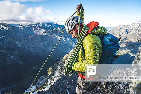 Mann mit Jacke und Rucksack wickelt Seil beim Klettern