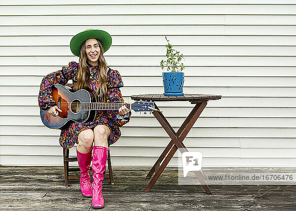Eine Frau sitzt allein an einem Holztisch an Deck und spielt akustische Gitarre