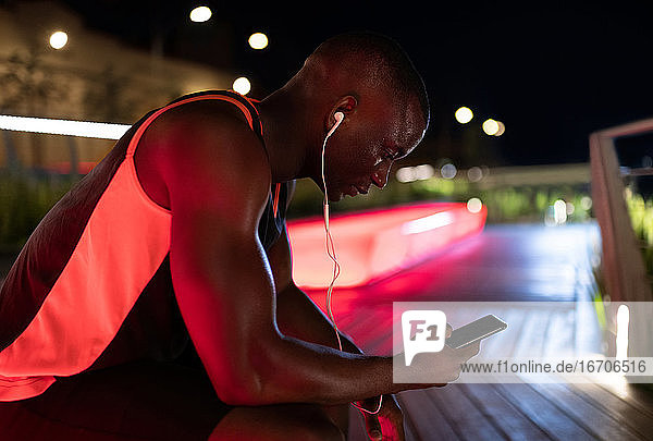 Schwarzer Läufer benutzt Smartphone auf Bank