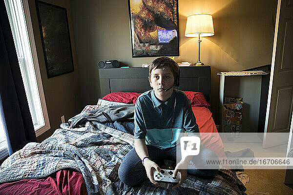 High View of Teen Boy Gaming While Wearing Headset  Sitting on Bed