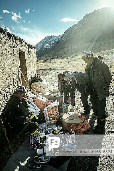 Händler breitet Elektrowaren  Medikamente  Batterien  Kleidung und Werkzeug auf dem Boden vor einem Steinhaus vor drei Männern aus  Khadz Goz  Wakhan-Korridor  Badachschan  Afghanistan  Asien