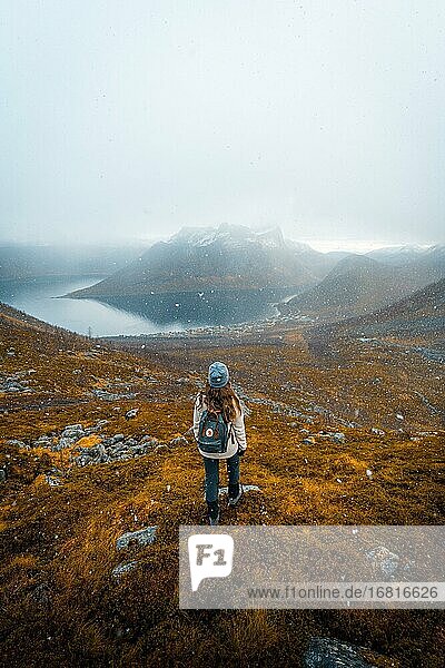Frau blickt auf den Ort Fjordbotn und einen markanten und spitzen Berg  Schneefall in herbstlicher Fjordlandschaft  Fjordgard  Senja  Norwegen  Europa