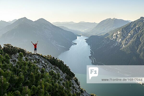 Young man stretches his arms into the air  view over mountain landscape  view from the top of the Bärenkopf to the Achensee  left Seekarspitze and Seebergspitze  Karwendel  Tyrol  Austria  Europe