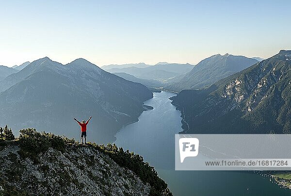 Junger Mann streckt die Arme in die Luft  Blick über Berglandschaft  Ausblick vom Gipfel des Bärenkopf auf den Achensee  links Seekarspitze und Seebergspitze  Karwendel  Tirol  Österreich  Europa
