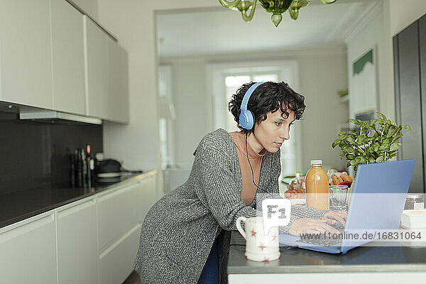 Frau mit Kopfhörer arbeiten von zu Hause aus am Laptop in der Küche