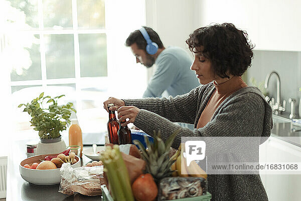 Frau entlädt Lebensmittel in der Küche  während der Ehemann am Laptop arbeitet