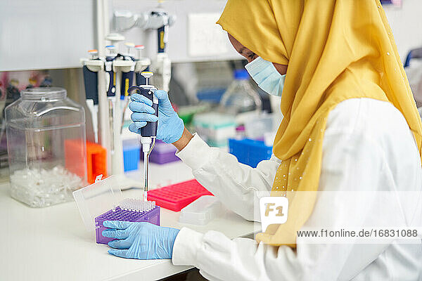 Weibliche Wissenschaftlerin in Hijab und Gesichtsmaske mit Pipette im Labor