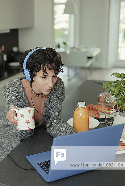 Frau mit Kopfhörer arbeiten von zu Hause aus am Laptop in der Küche am Morgen