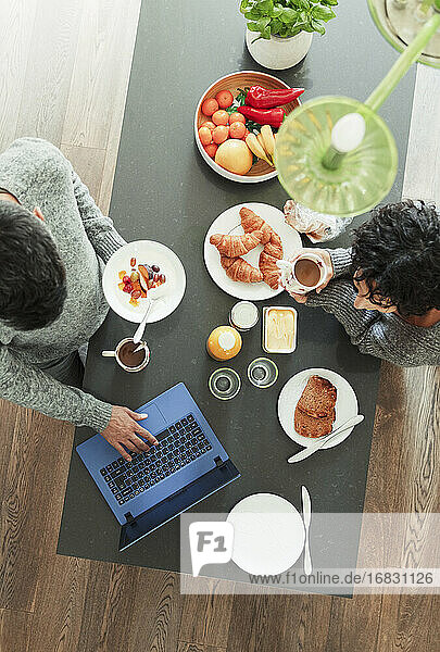 Paar genießt das Frühstück und arbeitet am Laptop in der Küche am Morgen