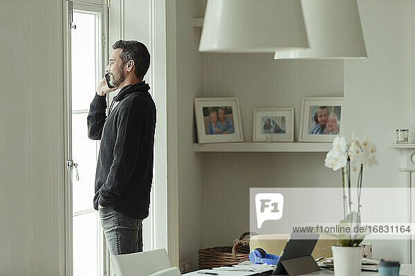 Mann spricht auf Smartphone am Esszimmerfenster