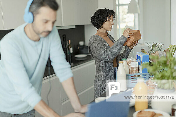 Couple working from home and unloading groceries in kitchen