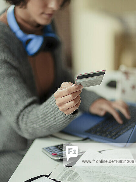 Frau mit Kreditkarte bezahlt Rechnungen online am Laptop
