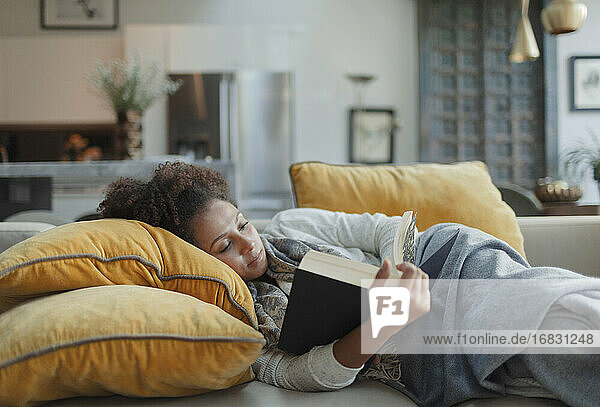 Woman relaxing and reading book on living room sofa