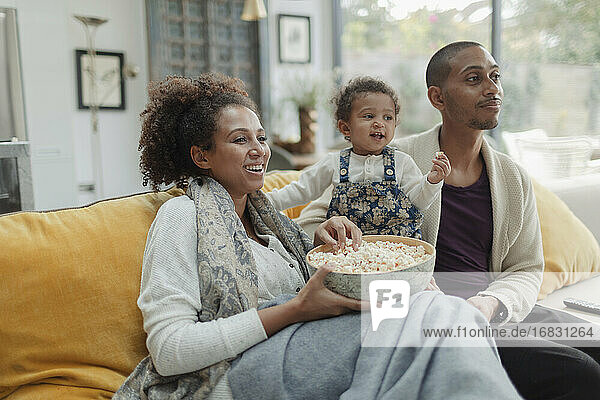 Paar mit Baby Tochter essen Popcorn und Fernsehen auf dem Sofa