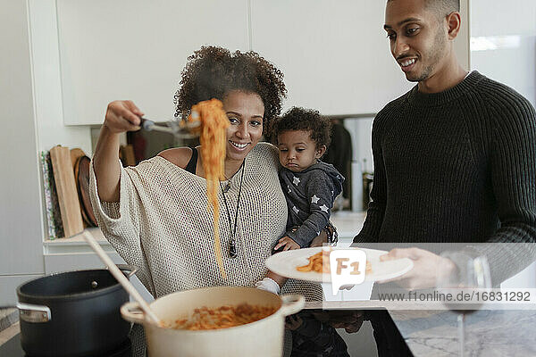 Parents with baby daughter cooking spaghetti at kitchen stove