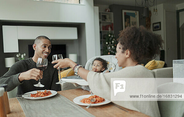 Happy couple with baby daughter enjoying wine and spaghetti dinner