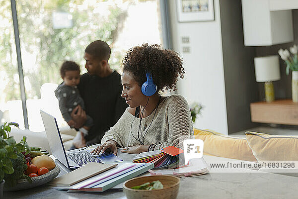 Frau arbeitet am Laptop im Esszimmer mit Ehemann und Baby Tochter