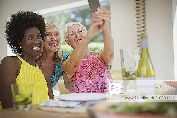 Senior women friends taking selfie at dining table