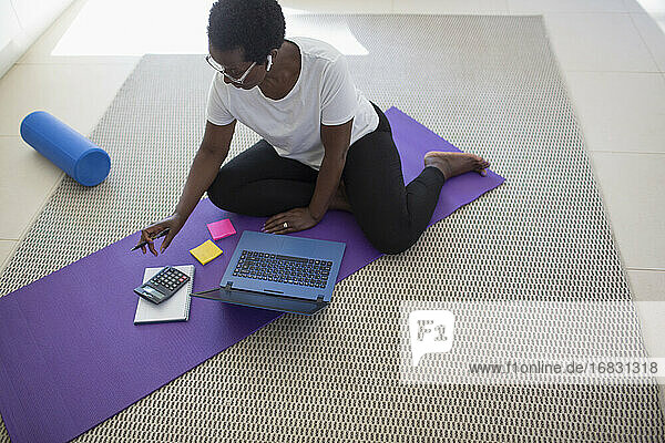 Reife Frau zahlt Rechnungen und arbeitet am Laptop auf Yogamatte