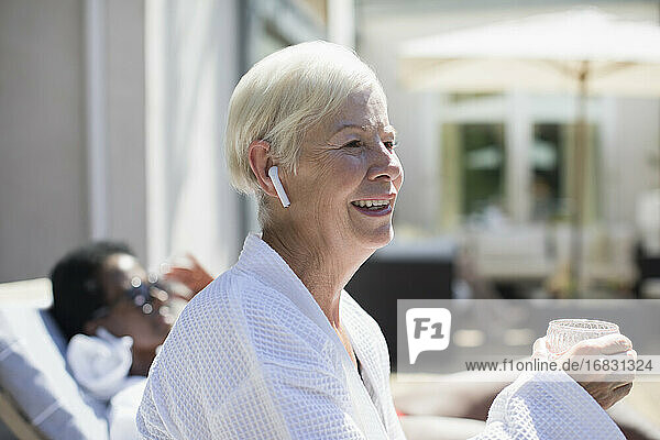 Glückliche ältere Frau mit Ohrstöpsel-Kopfhörer auf der sonnigen Hotelterrasse