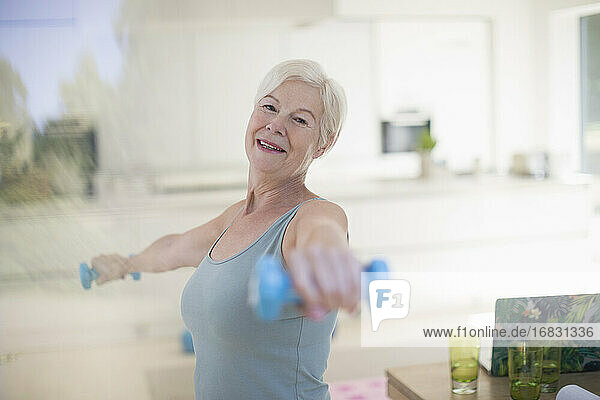Porträt selbstbewusste ältere Frau  die mit Hanteln in der Küche trainiert