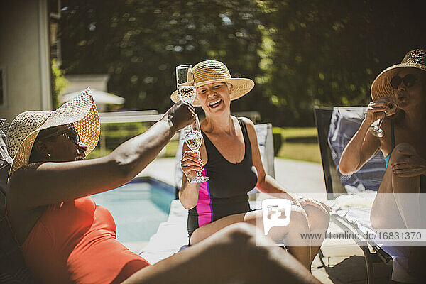 Happy senior women friends toasting champagne at sunny poolside