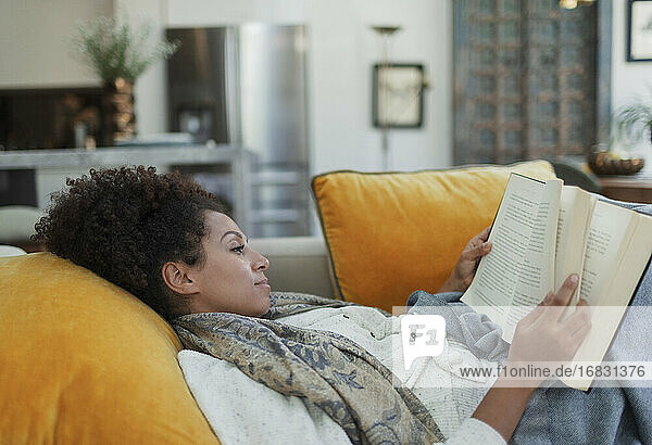 Serene woman reading book on living room sofa