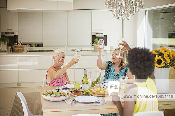 Glückliche Seniorinnen stoßen beim Mittagessen mit Weingläsern an